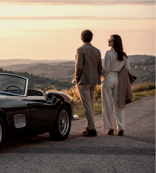 Elegant couple beside a vintage car on a Chianti road at sunset