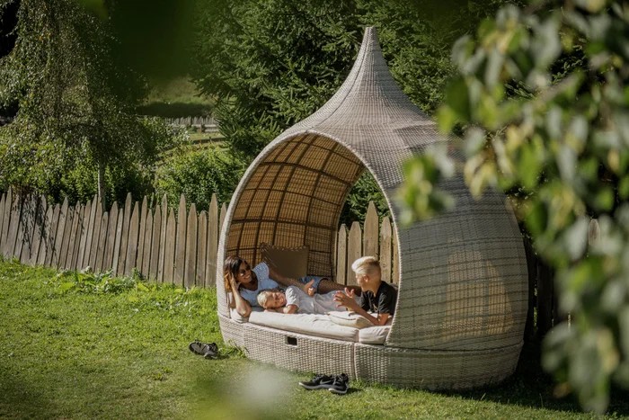 Family relaxing in an outdoor wicker daybed on the lawn