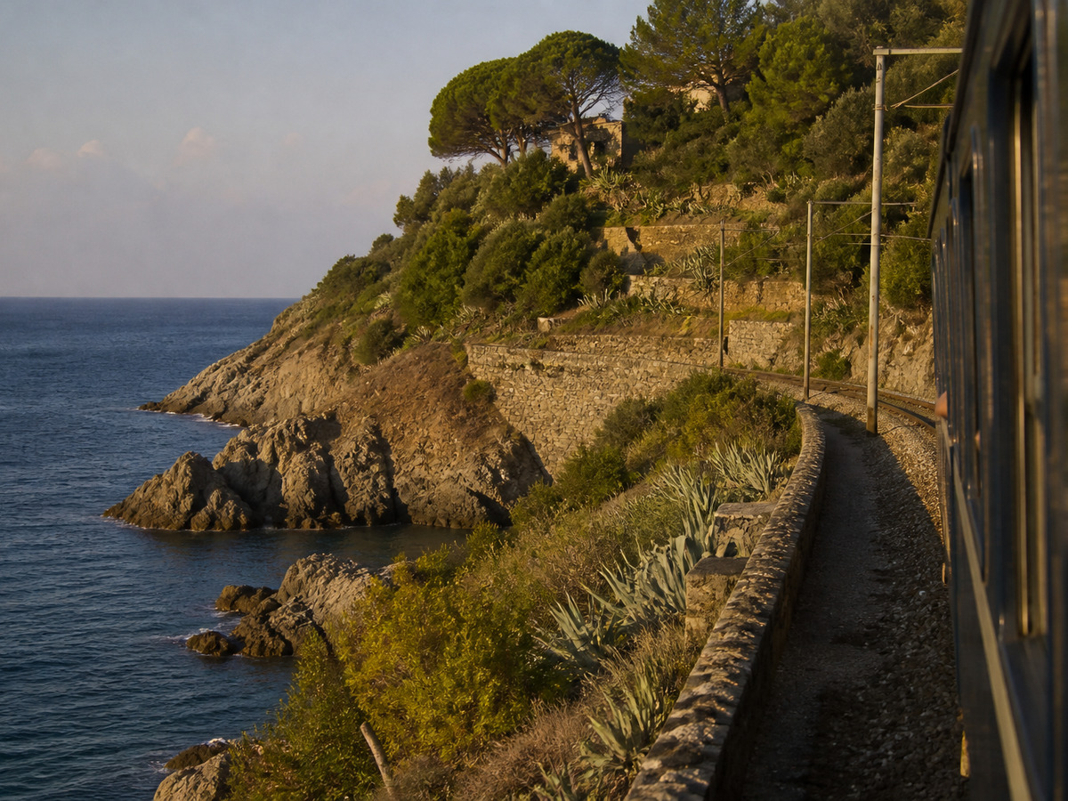 Coastal railway along the Ligurian shore at golden hour — editorial visual of entering Italy
