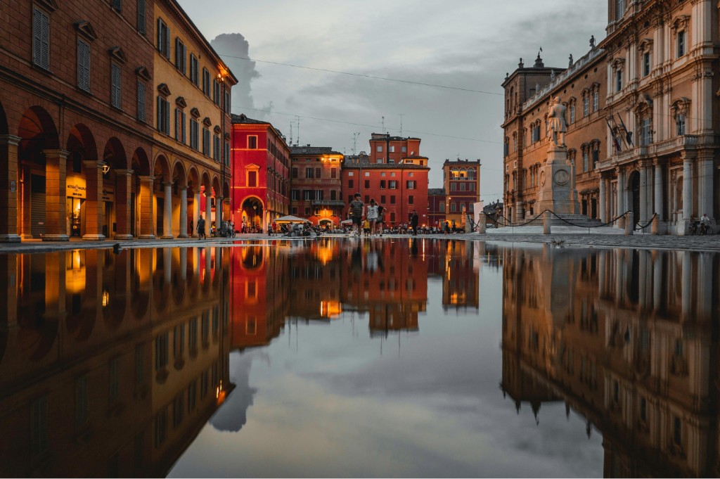 Modena’s Piazza Roma at dusk, porticoes and the ducal palace reflected in wet stone, Emilia-Romagna, OHH! ITALY