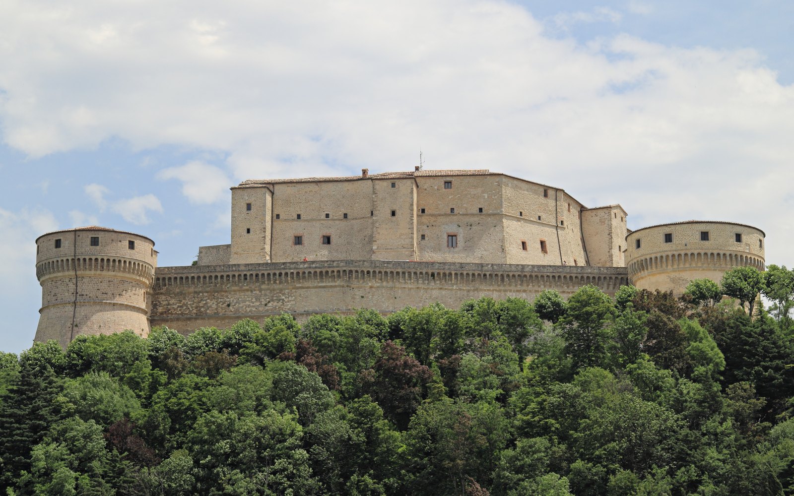 The fortress of San Leo, pale stone above a belt of trees, Emilia-Romagna, OHH! ITALY